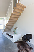Floating wooden staircase with integrated shelving, round armchair and fur rug