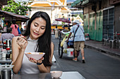 A young East Asian woman eating savoury congee (rice porridge) for breakfast