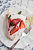 Piece of Pavlova cake with fresh strawberries garnished with mint leaves and elderflower