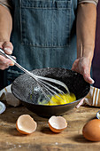 Whipping eggs in black bowl on wooden table with lemon , flour, butter and cinnamon sticks ingredients for cake