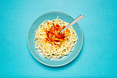 Blue ceramic plate with pasta and tomato sauce on light blue background