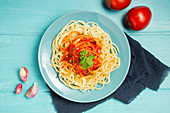 Blue ceramic plate with pasta and tomato sauce decorated with parsley and basil