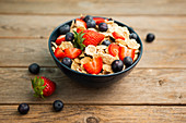 Breakfast bowl of corn flakes with strawberries and blueberries placed on wooden background