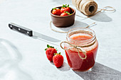 Fresh homemade strawberry juice in glass jar wrapped with twine placed on marble surface