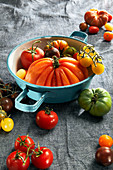 Various colourful tomatoes with an enamel colander on a tea towel