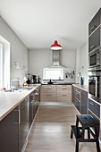Grey, modern kitchen with accent of colour provided by red ceiling lamp