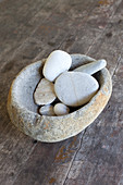 Pebbles in stone bowl on wooden floor
