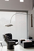 Arc lamp above black designer armchair next to window