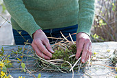 Woman winds wreath as an Easter basket made of moss and grass