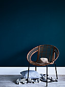 Hut auf Sessel mit Bespannung, darunter Kissen und Decke vor blauer Wand