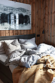 Rumpled bed in cosy bedroom with wood-clad walls