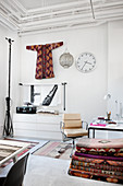 Classic chair, stack of kilim rugs and kimono hung on wall in white-painted study