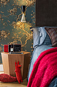 Reading lamp on hexagonal bedside table and bed against floral wallpaper