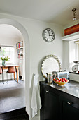 Base cabinet and wall clock next to arched open doorway in kitchen