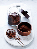 Kakaopulver in Glas, Schälchen und Küchensieb