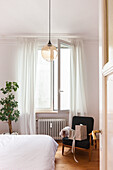 Bedroom with white bed linen, black armchair and glass pendant light