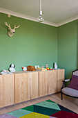 Wooden sideboard with toys in children's room with green walls and colorful carpet