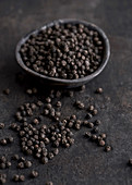 Black peppercorns in a black wooden bowl and on a black metal surface