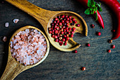 Salz, rote Pfefferkörner und Chilischoten auf Holzuntergrund