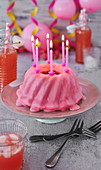 Pinker Gugelhupf zum Geburtstag mit rosa Luftballons, Luftschlangen und Kerzen