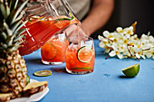 Ananas-Hibiskus-Cocktail aus Krug in Gläser einschenken