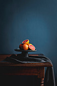 Pink grapefruit, whole and halved on a cake stand against a dark background