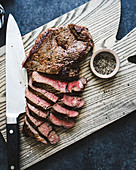 Sliced beef steak on a chopping board, along with knife