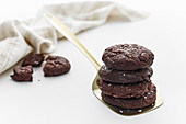A stack of double chocolate cookies on a gold spatula with broken cookie and linen in the background.