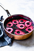 Red wine poached pear halves in a pan.