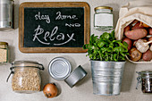 Flat lay of food supplies crisis for quarantine isolation period. Different glass jars with grains, cans of canned food, vegetables, chalkboard handwritten lettering Stay home and relax.