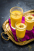 Three glasses of Mango Lassi garnished with saffron and crushed pistachio