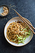 Udon noodles with peanut sauce and cucumber sticks in a bowl with chopsticks.