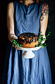 Frau im blauen Kleid hält Kuchenständer mit Blaubeerkuchen