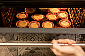 From above anonymous person opening hot oven and checking cupcakes while preparing pastry at home