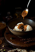 Caramel sauce being drizzled from a spoon onto vanilla ice cream in a bowl