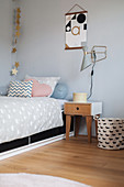 Scatter cushions on bed and bedside table below wall-mounted lamp in child's bedroom