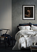 Nude painting on wall above double bed and classic chair in bedroom with grey walls