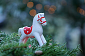 Red-and-white rocking horse ornament on fir branches against blurred background