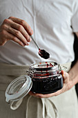 Man is holding a jar of blueberry jam in his hands