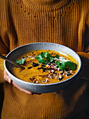 Woman holding spice-roasted pumpkin soup with macadamia dukkah