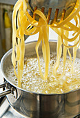 Italian pasta on metal tweezers pulled out of stainless steel pot