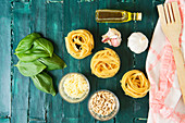 Dry pasta rolls near bowl with pesto sauce and fresh basil leaves with crushed garlic and pine nuts