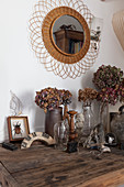 Vases of dried flowers on old wooden table below mirror on wall