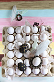 Painted eggs, feathers and twig on crate of white eggs
