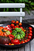 Various types of tomatoes - outdoor table and chair, with an antique colander