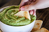 Woman's hand dipping pita bread into vegan avocado hummus