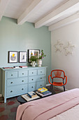 Pale blue chest of drawers against duck-egg-blue wall in bedroom with white ceiling beams