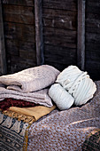 Stapel gefaltete Decken, Garnrolle und Wollknäuel vor Bretterwand