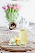 Flasche mit Limonade, Glas, Zitrone und Limette auf einem Holzbrett