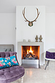 Antlers above fireplace in living room with purple easy chair in foreground